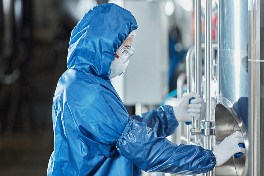 Personnel in full PPE completing lab work under a hood